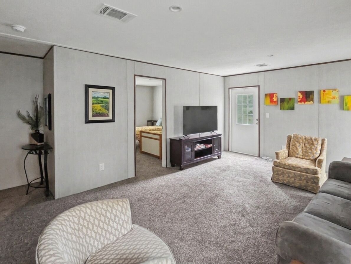 A living room with a flat-screen TV, a sofa, a patterned armchair, and a small table with a plant.