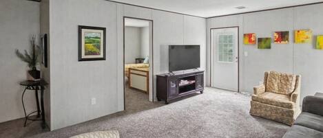 A living room with a flat-screen TV, a sofa, a patterned armchair, and a small table with a plant.
