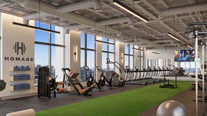 Une salle de sport moderne équipée de matériel d’exercice, dotée d’un espace recouvert de gazon synthétique et de grandes fenêtres offrant une vue sur la ville.
