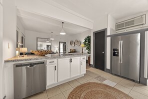 A modern kitchen with a dishwasher, stainless steel refrigerator, and a large island with a sink.
