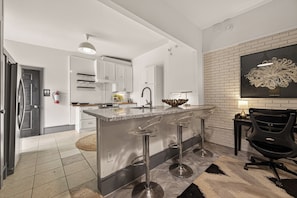 A modern kitchen with a central island, stainless steel bar stools, and a black office chair.