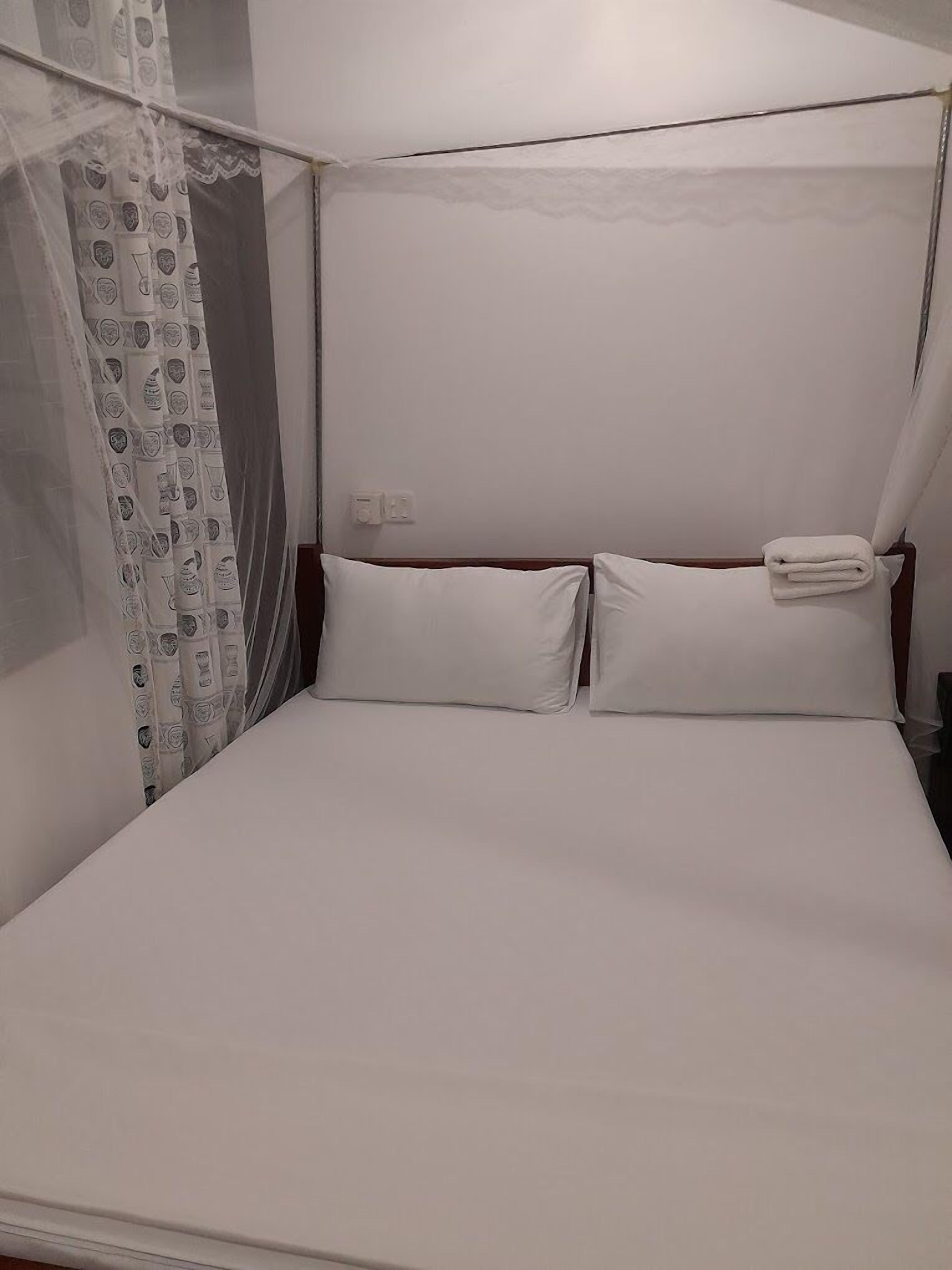 A single bed with white linens, a mosquito net, and a curtain with a pattern.