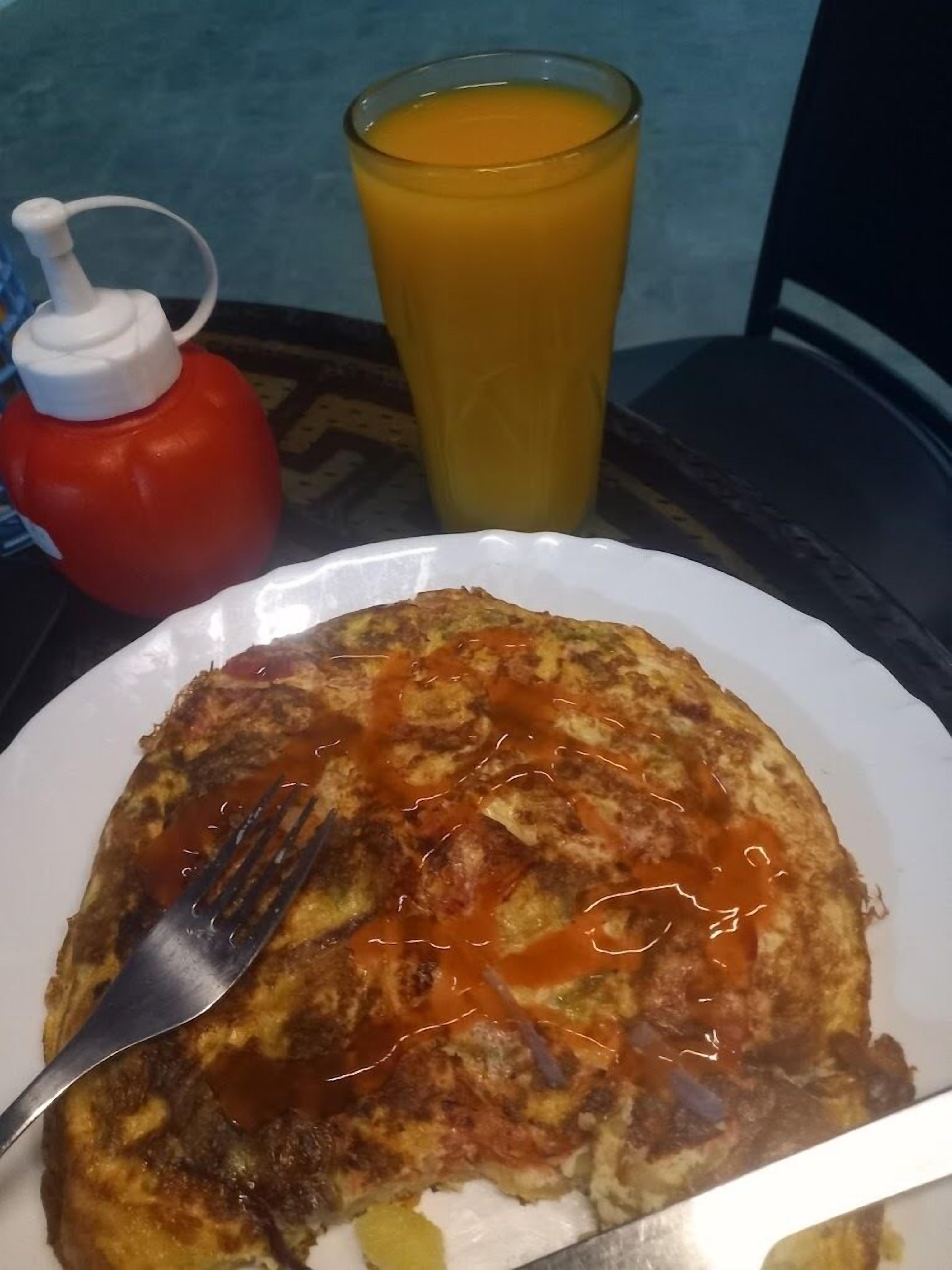 Un plato de comida con un tenedor, un vaso de jugo de naranja y una botella de kétchup sobre una mesa.