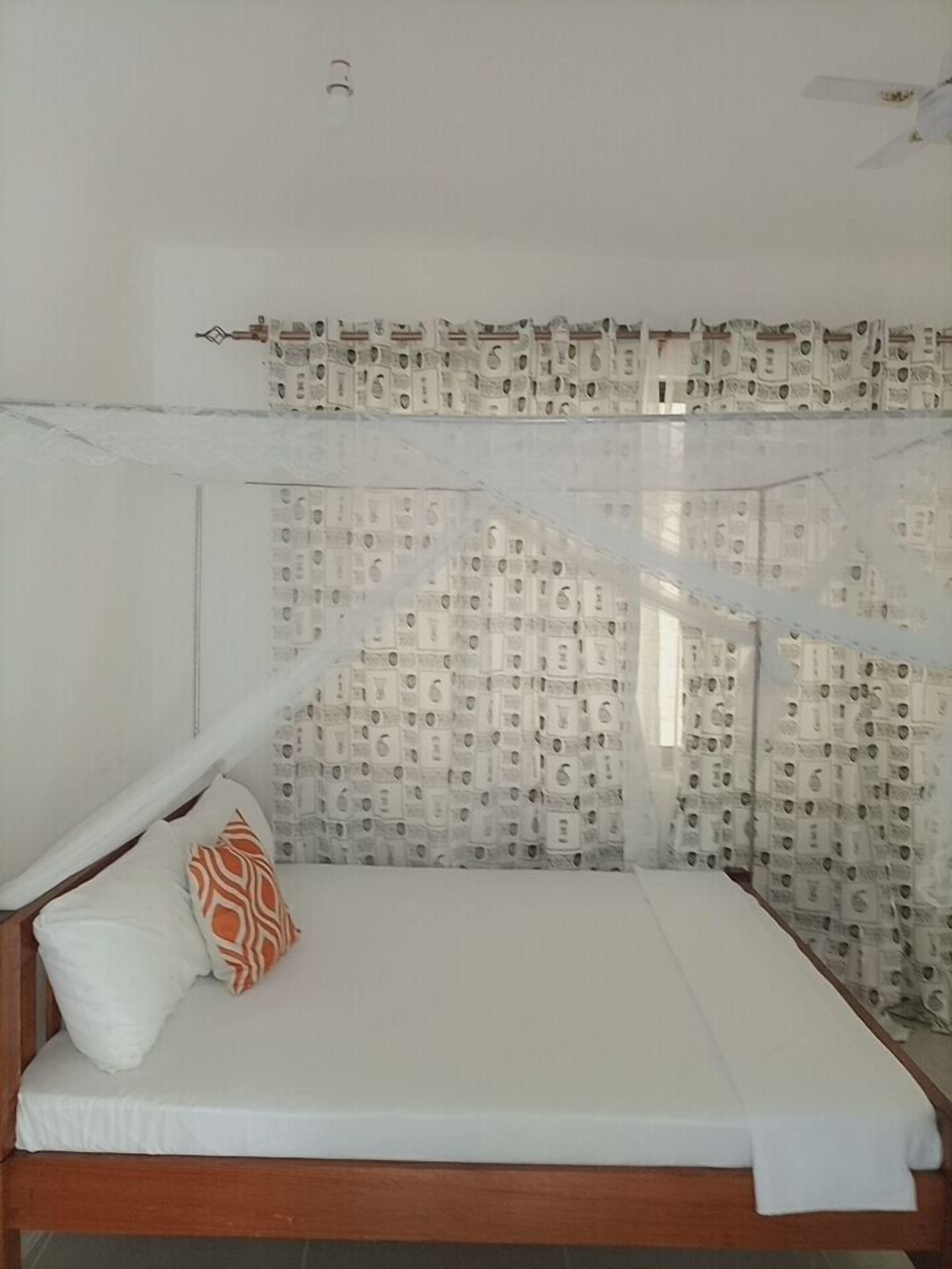Una cama individual con dosel, ropa de cama blanca y cortinas estampadas.