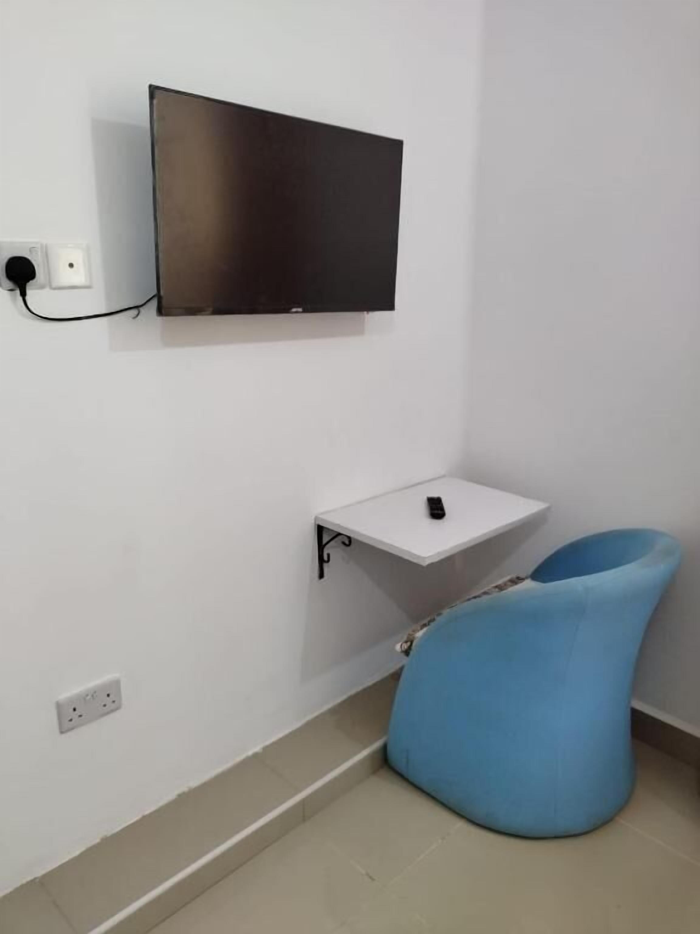 A room with a flat-screen TV mounted on the wall, a small white table with a remote control, and a blue bean bag chair.