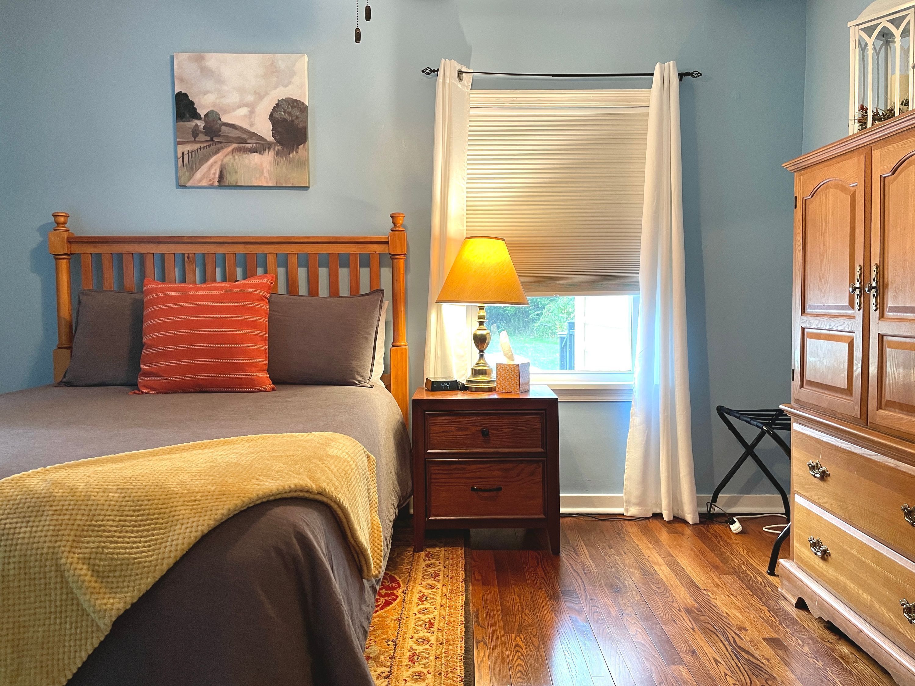Un dormitorio con cama, mesita de noche, lámpara y cómoda de madera.