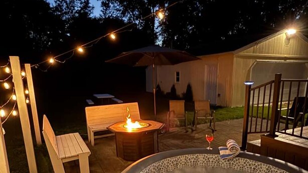 An outdoor hot tub area with a wooden bench, a small table with a candle, and string lights. - Hot Tub Outdoor Living Game Room Coffee Bar (South Bend)