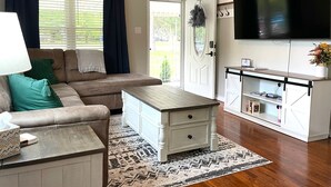 A living room with a sofa, a coffee table, a TV, and a door leading outside. - Hot Tub Outdoor Living Game Room Coffee Bar (South Bend)