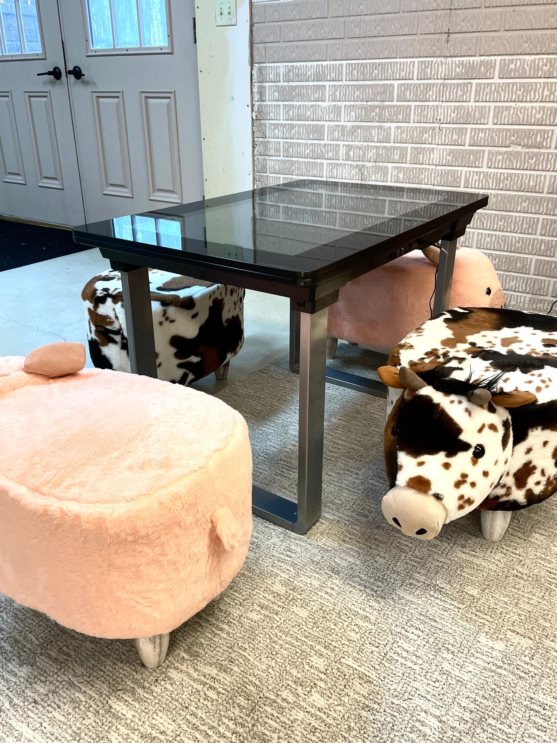 Una habitación con una mesa de vidrio, una puerta blanca, un muro con diseño de ladrillo y un otomano rosa.