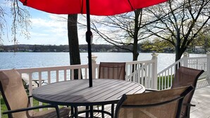 Une terrasse avec une table ronde et des chaises, un parasol rouge et une vue sur un lac.