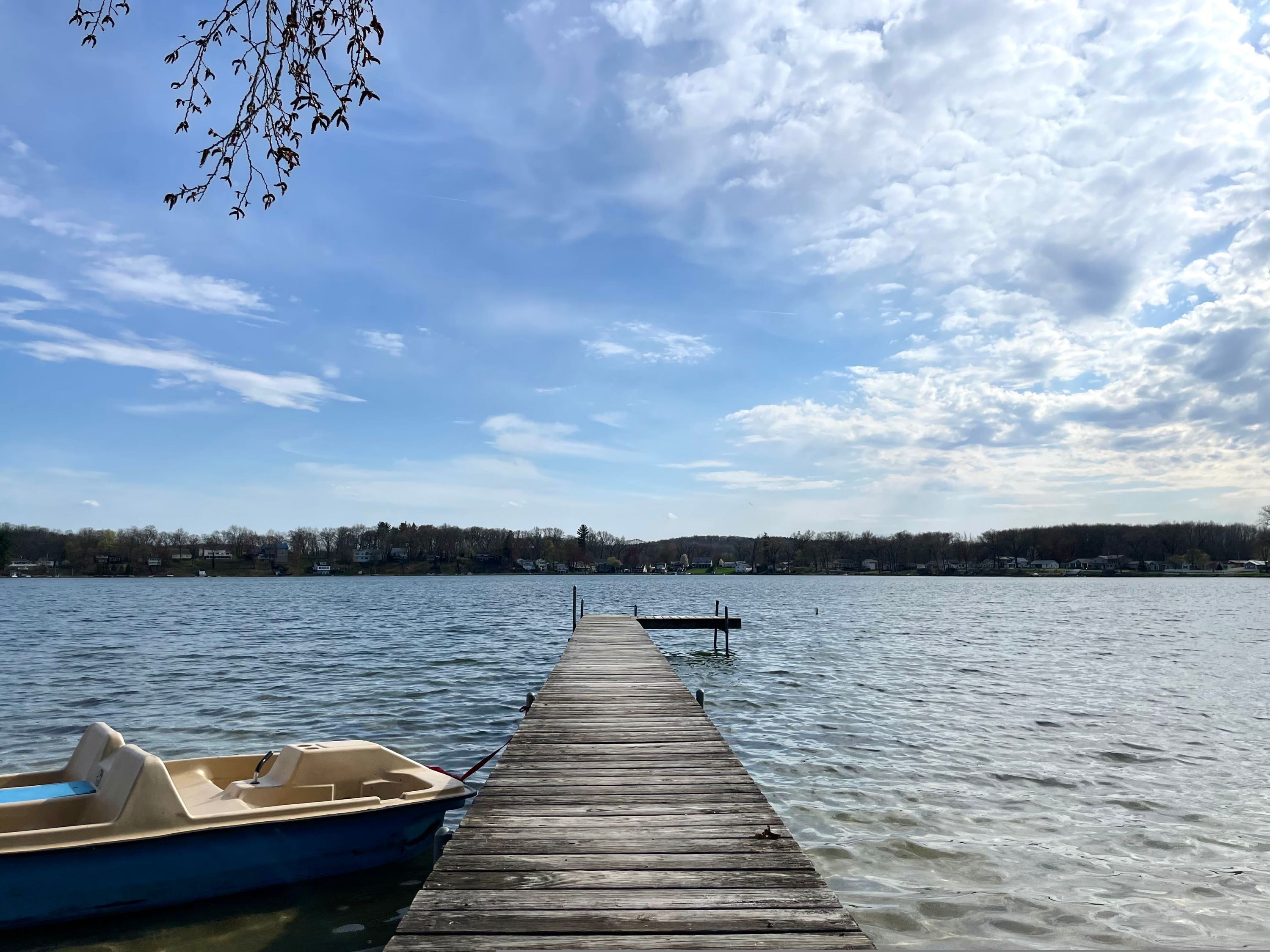 A wooden dock extending into a calm lake with a small boat docked at the end.