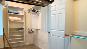 Un dressing avec plusieurs étagères, une tringle à vêtements et une porte dotée d’un interrupteur.