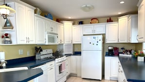 Une cuisine avec des meubles blancs, une cuisinière, un four à micro-ondes et un réfrigérateur.