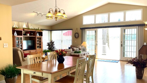 Un salon spacieux avec une table à manger en bois, des chaises, un téléviseur et une grande fenêtre avec des rideaux.
