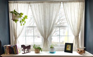 A window with sheer curtains, a potted plant, a wooden horse decoration, and a framed picture on a windowsill.