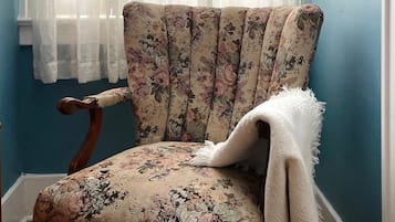 Una poltrona con rivestimento floreale in una stanza con pareti azzurre e una finestra con tende leggere.