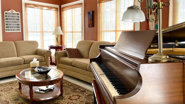 Un salon comprenant un piano à queue, deux canapés, une table basse en verre et un tapis à motifs.
