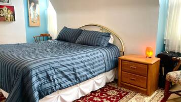 A bedroom with a bed, bedside table, lamp, chair, and a red and white patterned rug.