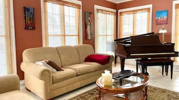 Una sala de estar con un sofá color beige, un piano de cola y una mesa de centro de vidrio.
