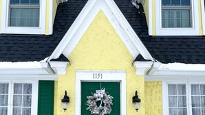 Een geel huis met een groene deur, nummer 1151, en een krans.