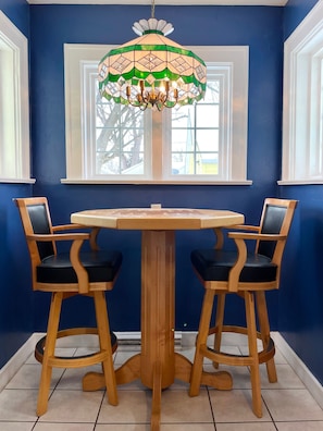 Un coin repas avec une table ronde en bois et quatre chaises en bois dotées de coussins noirs. Un lustre en vitrail est suspendu au-dessus de la table.