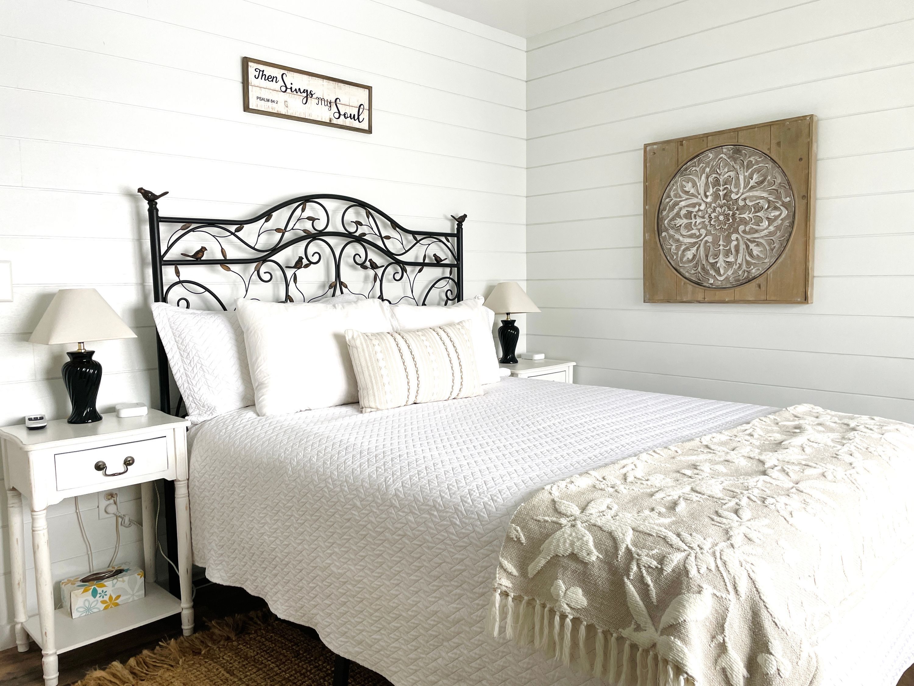 Une chambre à coucher bien rangée, avec un lit blanc, deux tables de chevet dotées de lampes, un élément décoratif mural et une œuvre d’art encadrée.