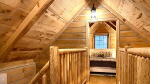 A wooden attic bedroom with a sloped ceiling, a bed, and a window. - Secluded Shipshewana Log Cabin In the Woods (Shipshewana)