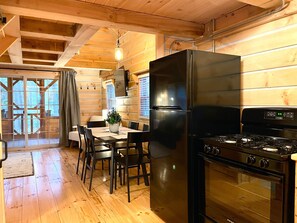 Ein Interieur einer Holzhütte mit Essbereich, einem schwarzen Kühlschrank und einem Herd.