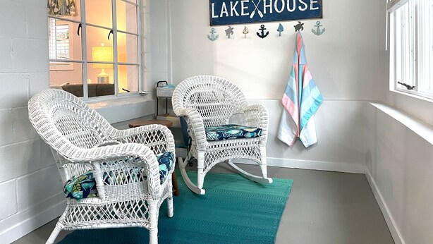 A cozy seating area with wicker chairs and a teal rug, a 'Welcome to our Lake House' sign, and nautical decorations. - Lake Front Cottage Kayaks Game Table Fun (Shipshewana)