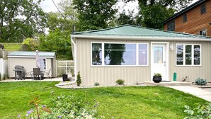 A single-story house with a green roof, a front porch, and a small garden area. - Lake Front Cottage Kayaks Game Table Fun (Shipshewana)
