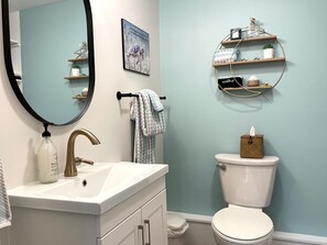 A bathroom with a white sink, a gold faucet, a mirror, a towel rack, a toilet, and a shelf with toiletries. - Lake Front Cottage Kayaks Game Table Fun (Shipshewana)