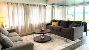 A living room with a ceiling fan, a sofa, a coffee table, and a view of the outdoors through large windows. - Lake House Kayaks Patio Deck Private Pier (Rome City)