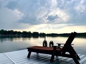 Eine Holzterrasse mit Liegestuhl und Tisch, mit Blick auf einen stillen See unter einem bewölkten Himmel.