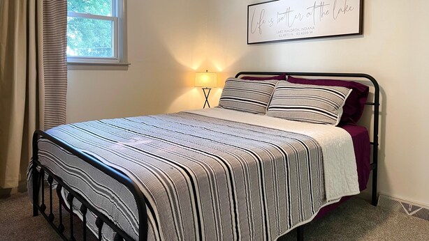 A bedroom with a bed, a window with curtains, a wall-mounted lamp, and a framed quote on the wall. - Lake House Kayaks Patio Deck Private Pier (Rome City)