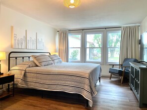 Ein Schlafzimmer mit Bett, Nachttisch, Lampe und Blick ins Freie durch große Fenster.