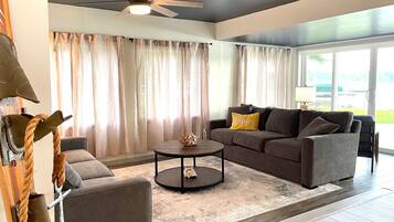 A modern living room with a ceiling fan, a sofa set, a coffee table, and a large window with curtains.
