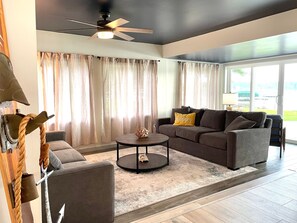 A modern living room with a ceiling fan, a sofa set, a coffee table, and a large window with curtains.