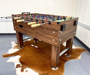 A wooden foosball table with metal rods and colorful balls, placed on a cowhide rug. - Lake House Kayaks Patio Deck Private Pier (Rome City)
