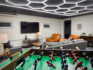 Un salon moderne doté d’un baby-foot, d’un grand téléviseur à écran plat et de sièges confortables.