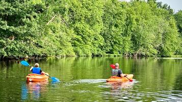Two people kayaking on a calm river surrounded by dense green foliage.