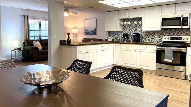A modern kitchen with white cabinets, a microwave, and an oven. There is a dining table with chairs and a decorative bowl. - Sarasota Family Home Private Heated Pool Relax (Sarasota)