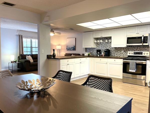 Une cuisine moderne avec des meubles blancs, un four à micro-ondes et un four traditionnel. On y trouve une table à manger avec des chaises et un bol décoratif.