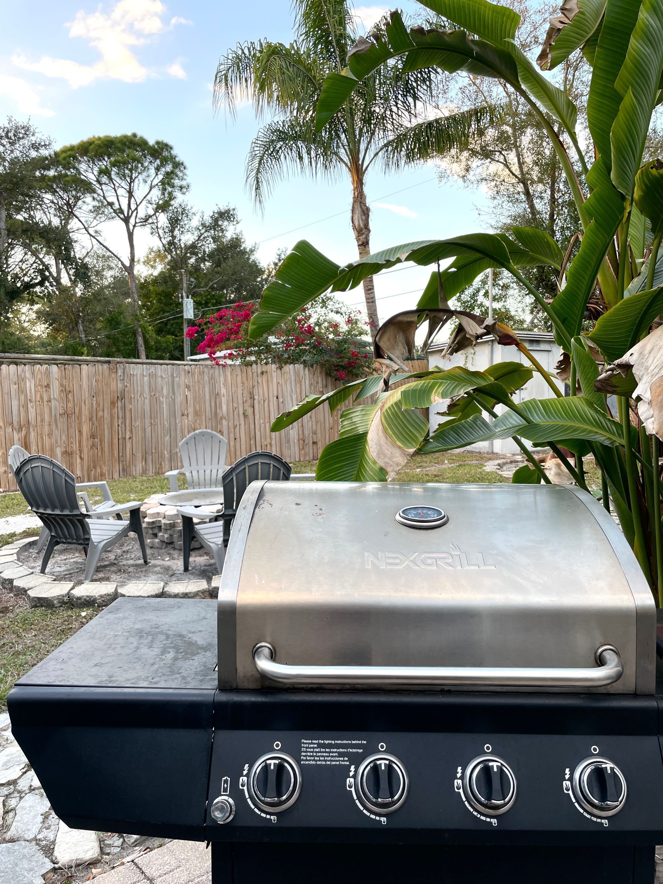 A barbecue grill with four controls, a wooden fence, and outdoor seating.