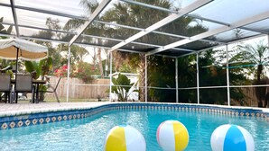 An indoor pool with three beach balls, a covered patio area, and a view of the surrounding garden. - Sarasota Family Home Private Heated Pool Relax (Sarasota)