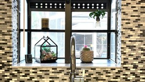 A kitchen with a large window, a stainless steel sink, and a decorative shelf with plants and a clock. - Sarasota Family Home Private Heated Pool Relax (Sarasota)