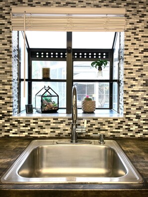 A kitchen with a large window, a stainless steel sink, and a decorative shelf with plants and a clock. - Sarasota Family Home Private Heated Pool Relax (Sarasota)