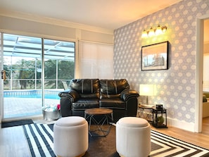Un salon moderne avec un canapé en cuir, des poufs, une petite table ronde et un mur décoré de motifs.
