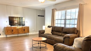 A modern living room with a brown leather sofa, a small round coffee table, and a television on a wooden cabinet. - Sarasota Family Home Private Heated Pool Relax (Sarasota)