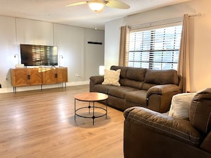 A modern living room with a brown leather sofa, a small round coffee table, and a television on a wooden cabinet. - Sarasota Family Home Private Heated Pool Relax (Sarasota)