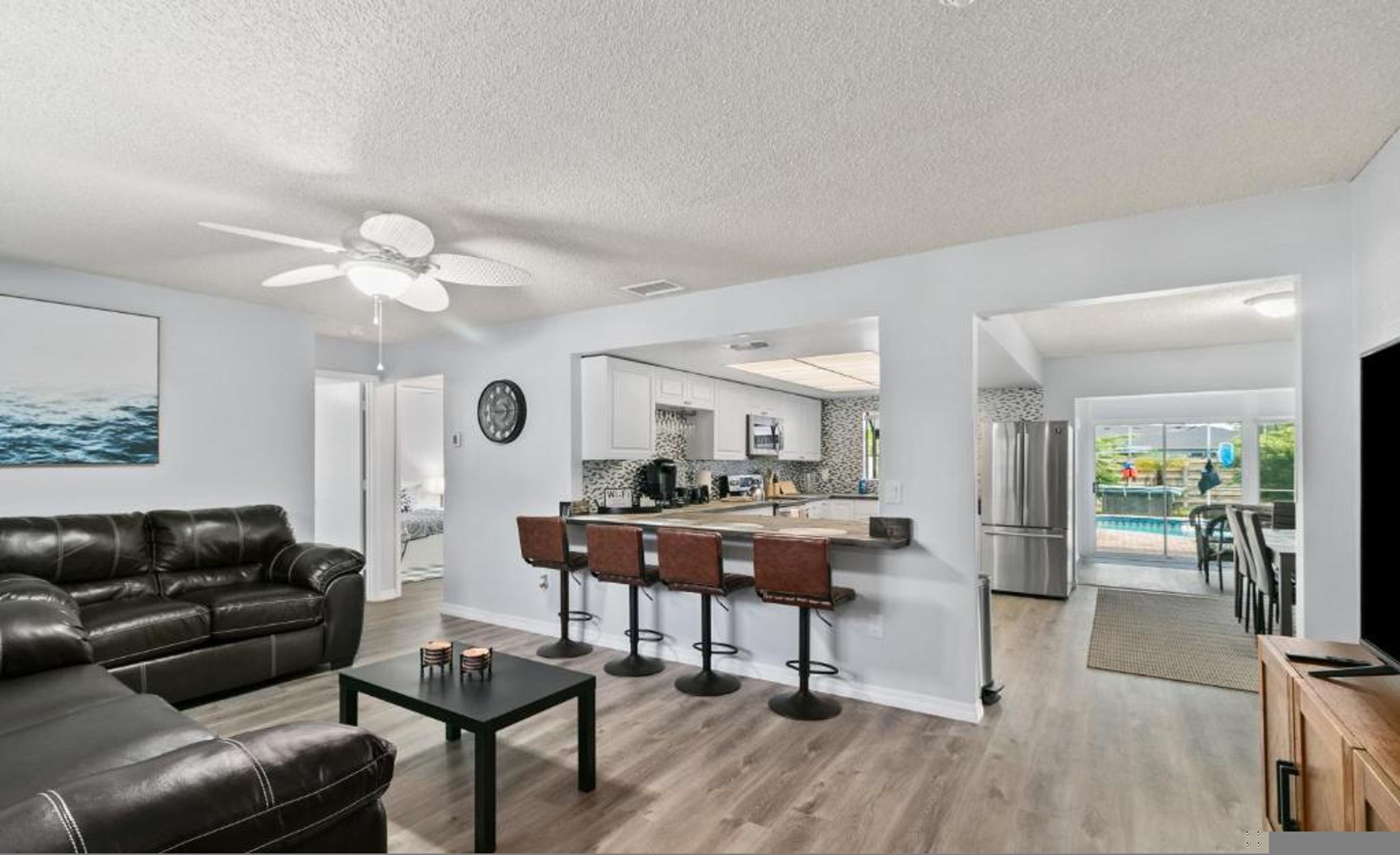 A modern living room with a black leather sofa, a coffee table, and a bar area with stools.